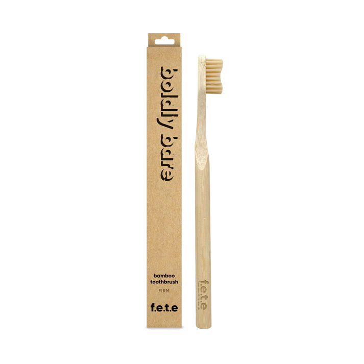 The F.E.T.E. Single Firm Bamboo Toothbrush is displayed next to its brown cardboard packaging, emphasizing its eco-friendly design, available at Fisa Health.
