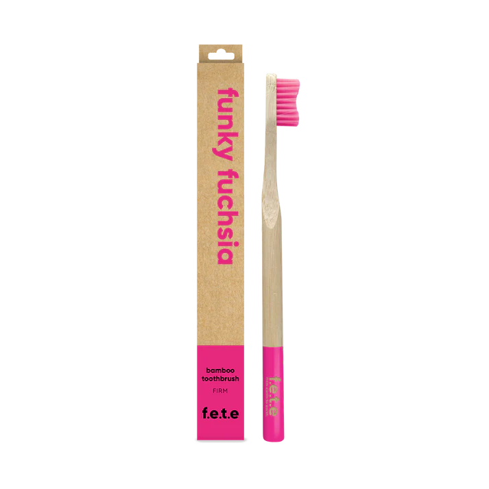 The F.E.T.E. Single Firm Bamboo Toothbrush with bright pink bristles and tip is shown next to its brown "funky fuchsia" box featuring pink text, available at Fisa Health.