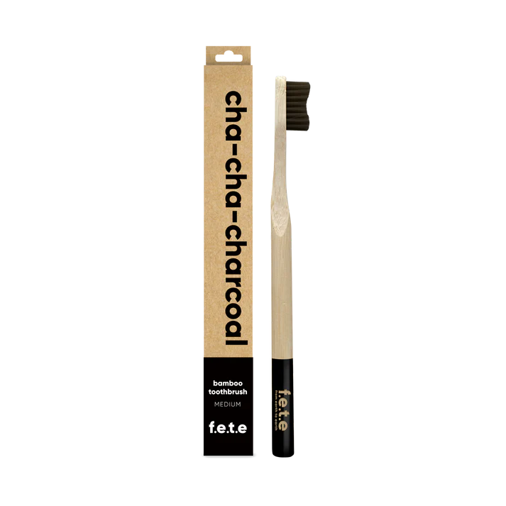 The F.E.T.E. Single Medium Bamboo Toothbrush features black bristles, a biodegradable handle, and is packaged in a “cha-cha-charcoal” box, available at Fisa Health.
