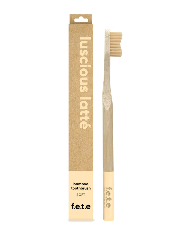 A F.E.T.E. Single Soft Bamboo Toothbrush with beige bristles is positioned beside its brown "luscious latté" eco-friendly packaging, available at Fisa Health.