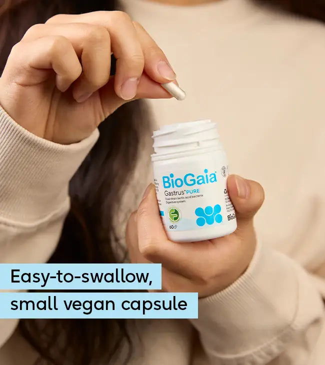 A person holds a white bottle labeled BioGaia® Gastrus® PURE, featuring FODMAP Friendly and vegan capsules in simple packaging, available at Fisa Health.