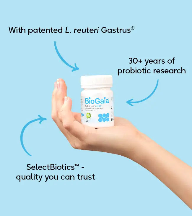 A hand holds a bottle of BioGaia® Gastrus® PURE. The label displays L. reuteri Gastrus®, 30+ years’ research, FODMAP Friendly, and SelectBiotics™ quality; blue arrows highlight these details, available at Fisa Health.