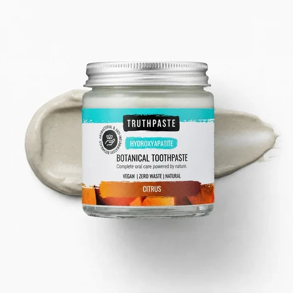 A jar of Truthpaste Hydroxyapatite: Citrus (100ml) rests on a citrus-colored smear, with packaging that highlights vegan and zero waste features, available at Fisa Health.