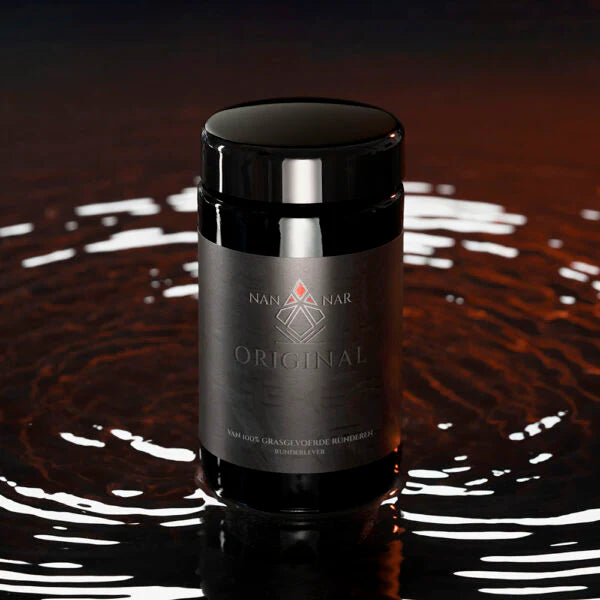 A black jar labeled Nannar Original, a grass-fed beef liver supplement, sits on a dark reflective surface with circular ripples around it, available at Fisa Health.