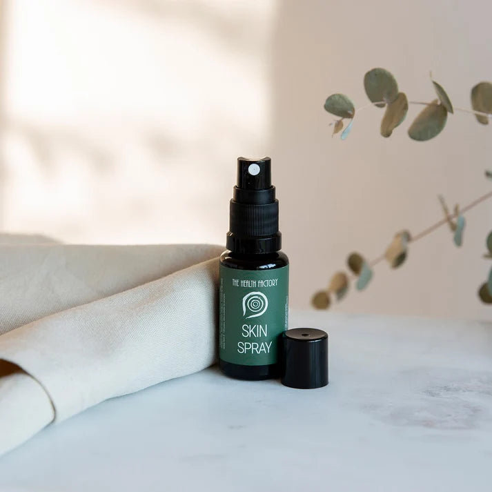 A small dark bottle labeled The Health Factory Nano Zinc Skin Spray 15ml sits on marble with its cap off, next to eucalyptus, available at Fisa Health.