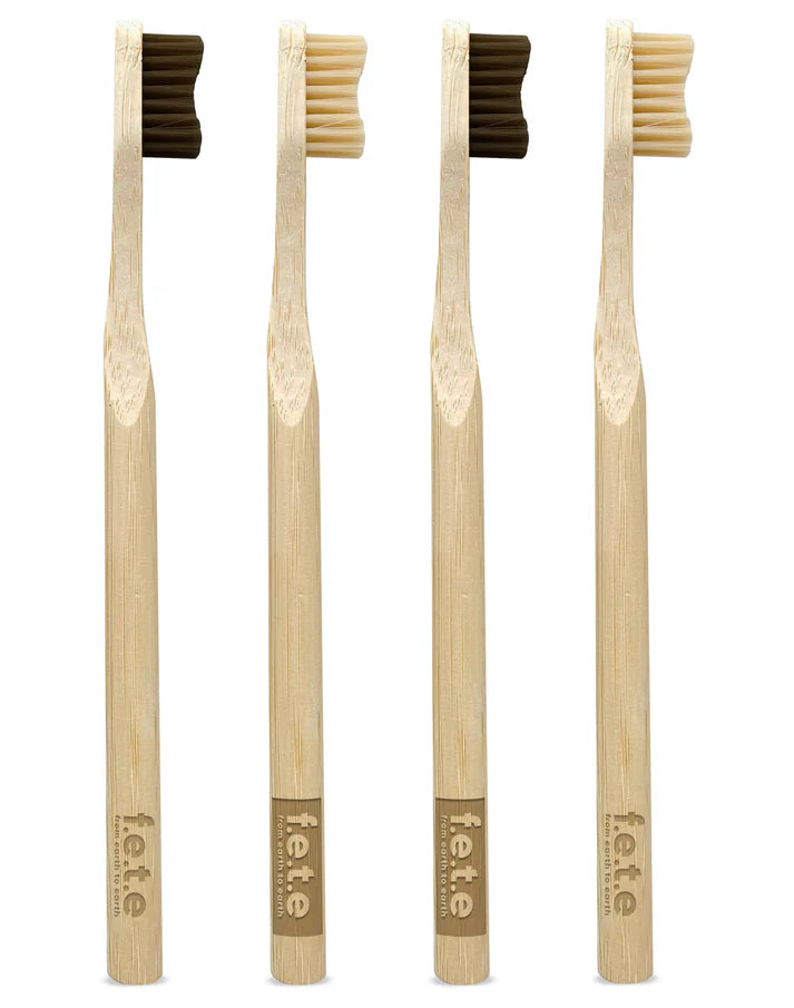 Four F.E.T.E. Natural Vegan Medium Bamboo Toothbrushes with charcoal bristles (pack of 4) stand upright on a white background, available at Fisa Health.