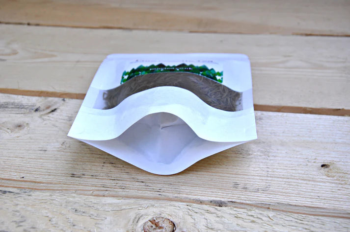A white resealable stand-up pouch labeled Pinetea sits on a light wooden surface, filled with dried Romanian pine needles, available at Fisa Health.