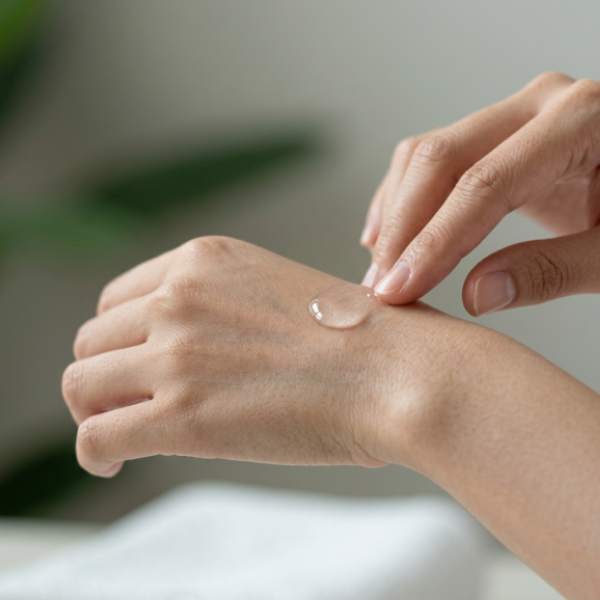 A person applies Skin Bundle gel or serum to the back of their hand with a fingertip, in front of a blurred background, available at Fisa Health.