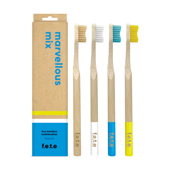 Four F.E.T.E. Multipack Medium Soft Bamboo Toothbrushes with colored bristles and handles are arranged beside their eco-friendly, biodegradable, plastic-free box of 4, available at Fisa Health.