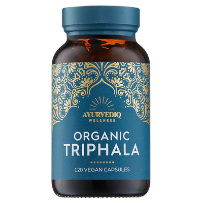 A brown bottle labeled Organic Triphala 120 Vegan Capsules sits against a blue background with gold patterns, available at Fisa Health.
