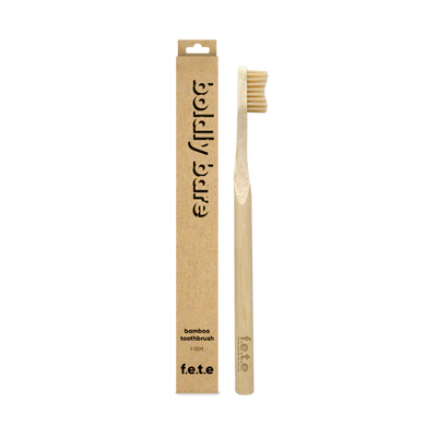 The F.E.T.E. Single Firm Bamboo Toothbrush is displayed next to its brown cardboard packaging, emphasizing its eco-friendly design, available at Fisa Health.