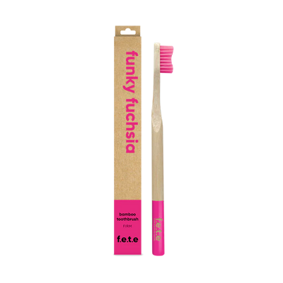 The F.E.T.E. Single Firm Bamboo Toothbrush with bright pink bristles and tip is shown next to its brown "funky fuchsia" box featuring pink text, available at Fisa Health.
