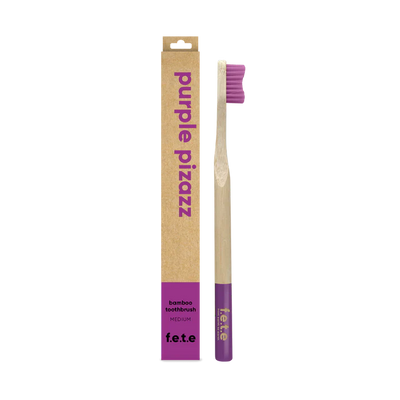 A F.E.T.E. Single Medium Bamboo Toothbrush with a biodegradable handle and purple bristles is shown next to its "purple pizazz" box, available at Fisa Health.