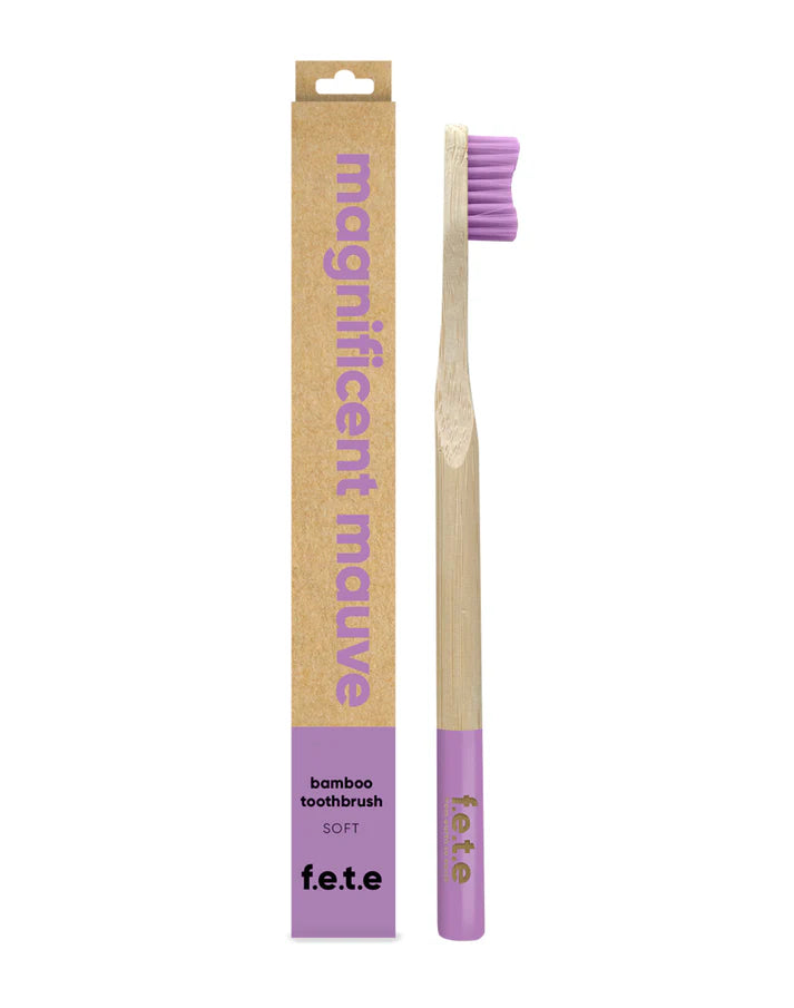 F.E.T.E. Single Soft Bamboo Toothbrush with a biodegradable handle, purple bristles, matching base, and eco-friendly "Magnificent Mauve" packaging, available at Fisa Health.