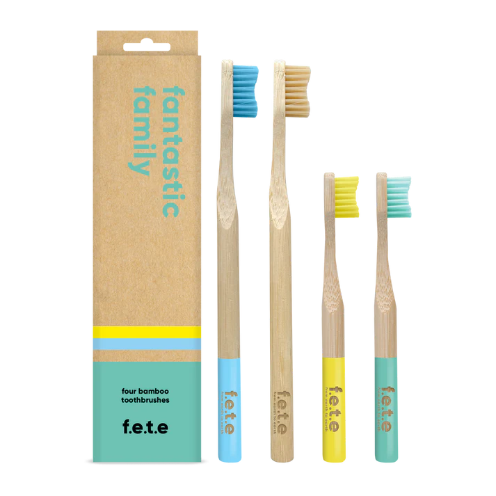 Four F.E.T.E. Family Pack bamboo toothbrushes (2 adult, 2 children) with blue and yellow handles are displayed next to the product box, available at Fisa Health.