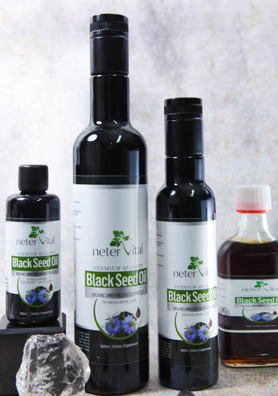 Four Neter Vital Black Seed Oil Cold-Pressed Nigella Sativa bottles are arranged upright beside a gray rock on a light surface with a neutral background, available at Fisa Health.