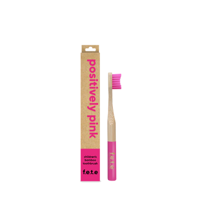 A pink and natural bamboo F.E.T.E. Children’s Bamboo Toothbrush stands upright beside its “positively pink” labeled cardboard box, available at Fisa Health.