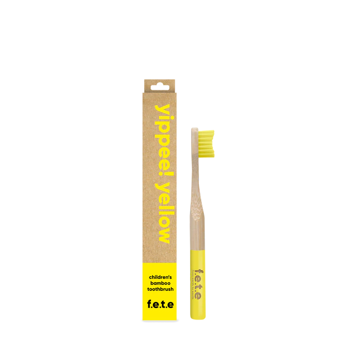 F.E.T.E. Children's Bamboo Toothbrush with yellow bristles and tip beside its box labeled “yippee! yellow” and “children’s bamboo toothbrush f.e.t.e.”, available at Fisa Health.