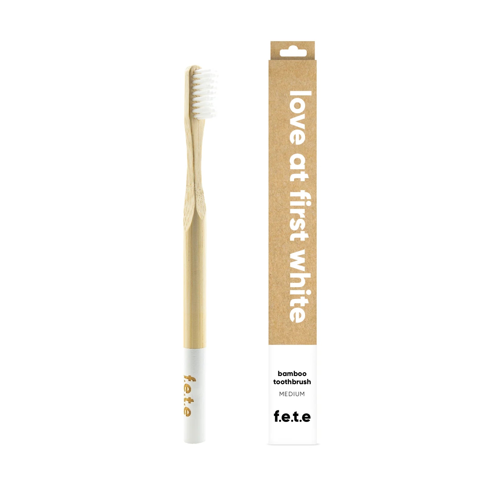 A biodegradable F.E.T.E. Single Medium Bamboo Toothbrush with white bristles is positioned next to its brown box labeled "love at first white", available at Fisa Health.