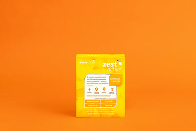 A yellow box labeled "Revive Zest Active - Orange" is centered on an orange background, with images of ingredients on the packaging. Available at Fisa Health.