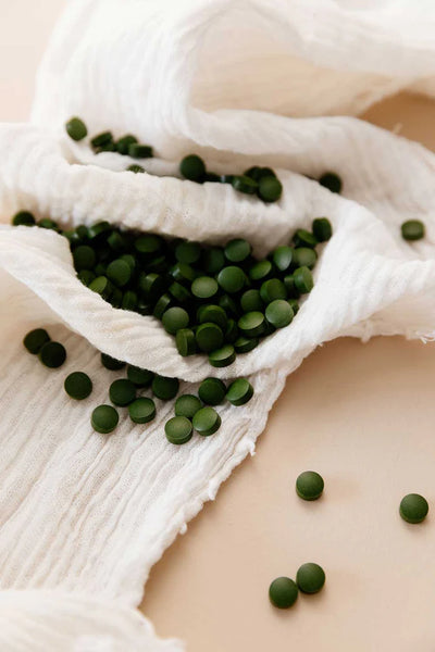 Fermented Chlorella Tablets X 240—small, round green tablets—are displayed on a crinkled white cloth, some gathered in clusters and others spread apart, available at Fisa Health.