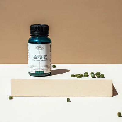A bottle of Fermented Chlorella Tablets X 240 is displayed on a beige platform with green tablets nearby, set against a minimalist brown and white background, available at Fisa Health.