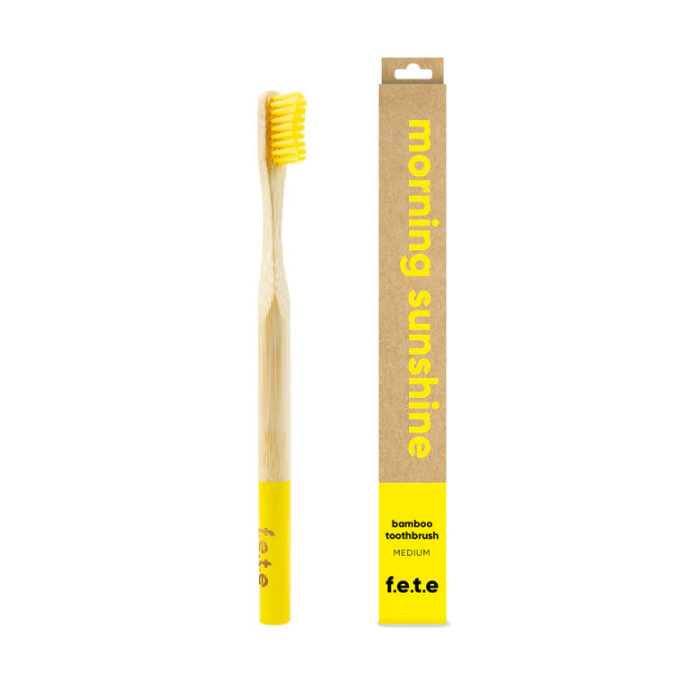 The F.E.T.E. Single Medium Bamboo Toothbrush has yellow bristles, a yellow-tipped handle, and is packaged in a brown box labeled "morning sunshine", available at Fisa Health.