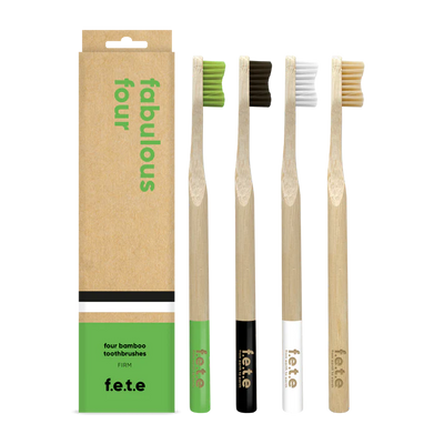 Four F.E.T.E. Multipack Firm Bamboo Toothbrushes in green, black, white, and natural are displayed next to a box labeled "fabulous four" and "four bamboo toothbrushes," available at Fisa Health.