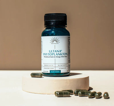 A bottle labeled Phytoplankton 60 Veg. Capsules (500mg) Omega & Multi, with green capsules displayed on a round platform against a beige background, available at Fisa Health.