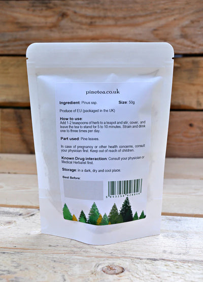 A white, resealable Pinetea packet made from Romanian pine needles stands upright on a wooden surface, displaying the back label with brewing instructions and product details, available at Fisa Health.
