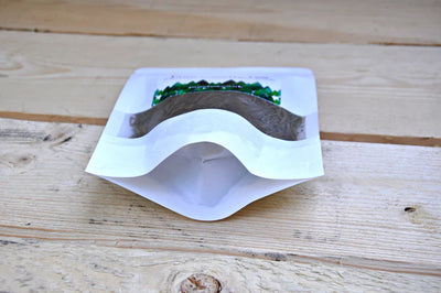 A white resealable stand-up pouch labeled Pinetea sits on a light wooden surface, filled with dried Romanian pine needles, available at Fisa Health.